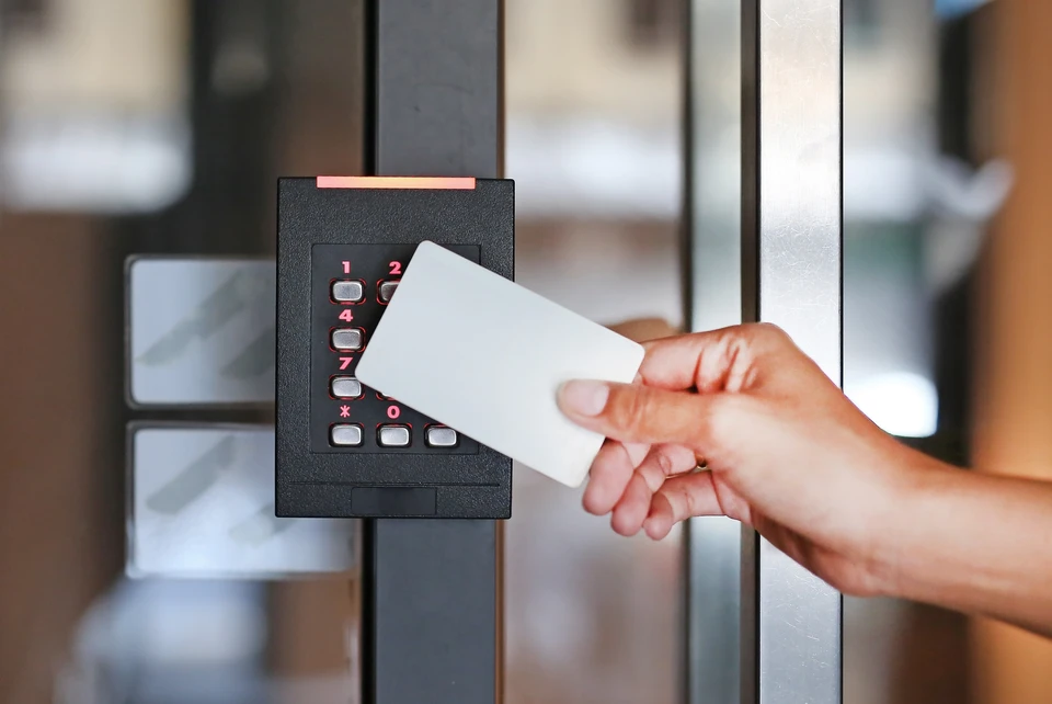 Une personne utilise un badge d'accès blanc pour déverrouiller une porte vitrée équipée d'un système de contrôle d'accès électronique