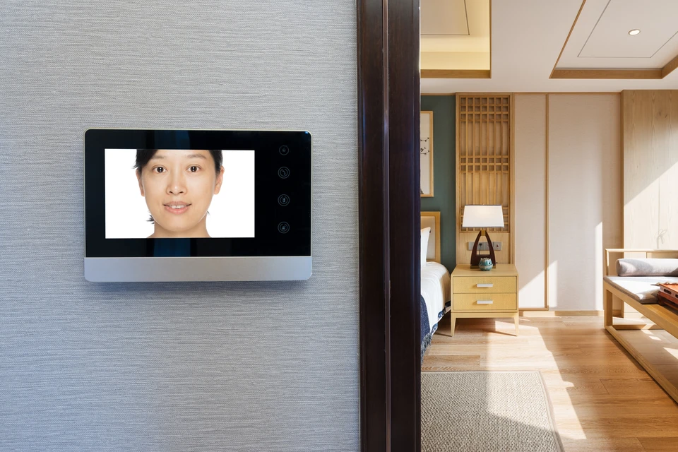 Intérieur résidentiel moderne avec écran d'interphone vidéo mural affichant le visage d'une femme asiatique souriante