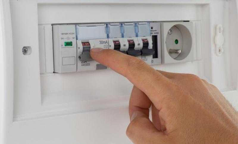 Électricien professionnel effectuant une vérification avec un multimètre sur un tableau électrique domestique blanc en rénovation résidentielle, dans un intérieur sans combinaison ostentatoire, concentré sur son diagnostic technique.