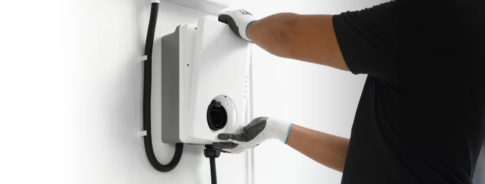 Un homme installe une prise de câble à sa voiture électrique avec une borne de recharge à domicile dans la cour arrière