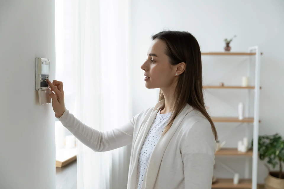 Radiateur électrique à inertie en fonte de couleur blanc cassé ou noir mat, installé sous une fenêtre dans une chambre lumineuse avec parquet clair, montrant le radiateur seul et complet depuis le bas jusqu'au-dessus du rebord de fenêtre, offrant une vue complète de sa silhouette et de sa structure.