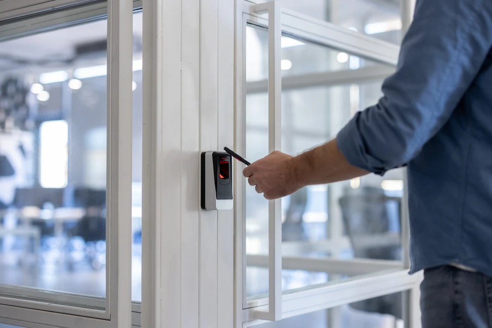 Électricien professionnel en tenue de travail raccordant des câbles de sécurité et domotique à un tableau électrique blanc moderne dans un local commercial, vue rapprochée des connexions et du matériel Hager ou Schneider Electric.