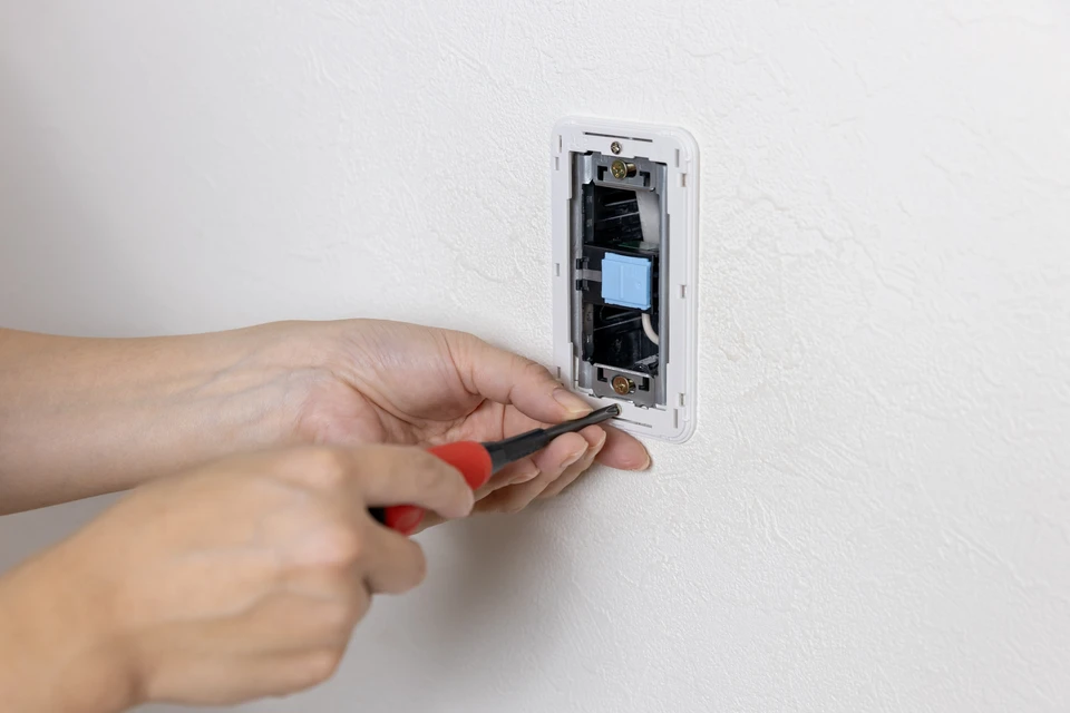 Électricien professionnel en gants de protection effectuant le raccordement des fils électriques et des disjoncteurs dans un tableau électrique mural blanc en armoire murale, mettant en évidence les connexions de sécurité en milieu résidentiel.