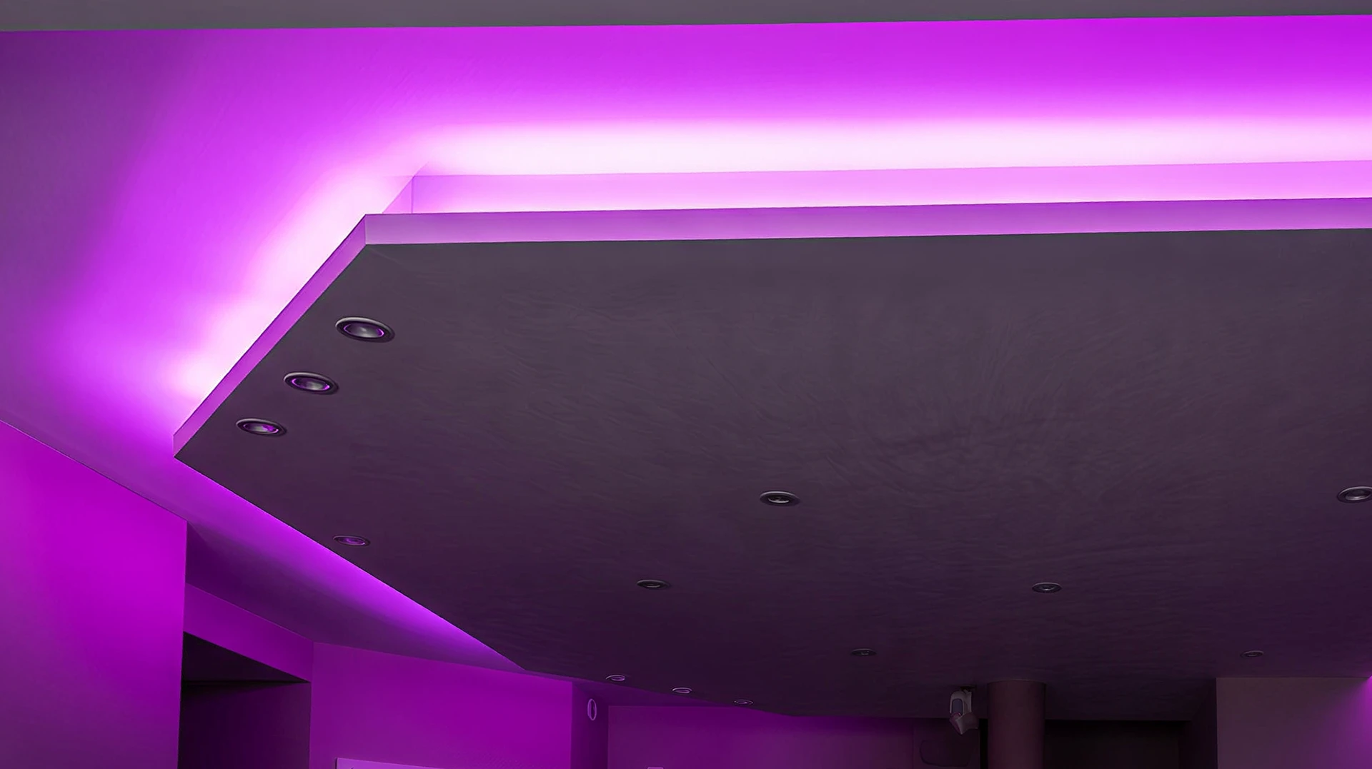 Électricien professionnel en tenue de travail installant un boîtier de commande domotique blanc moderne fixé au mur intérieur d'une maison. L'électricien utilise un tournevis pour connecter les fils de câblage dans le boîtier, mur peint en couleur neutre, intérieur résidentiel contemporain visible en arrière-plan.